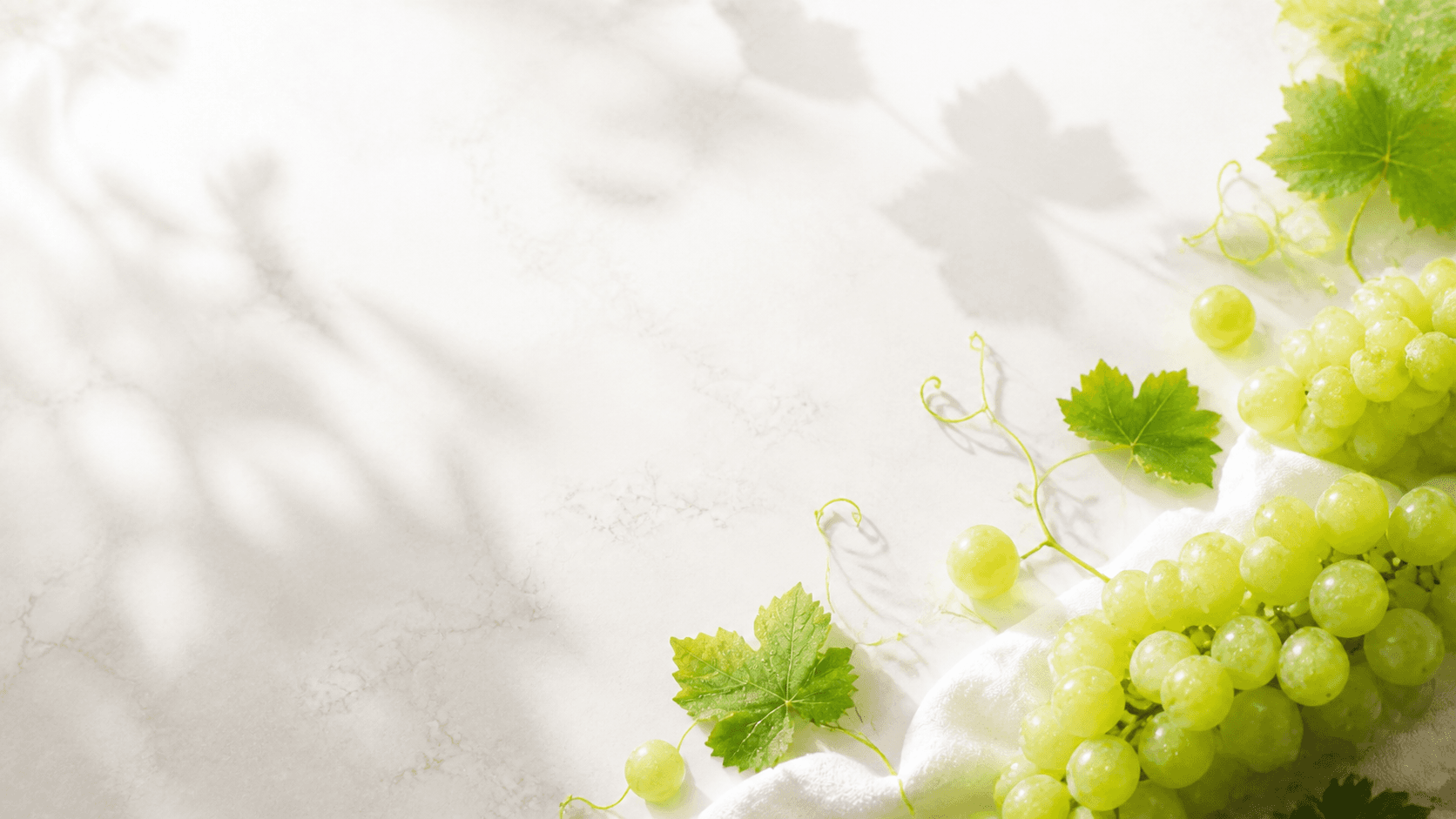 Fresh green grapes and vine leaves on a luminous stone surface